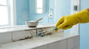 Main gantée nettoyant précisément un joint de douche encrassé avec une brosse pour illustrer comment nettoyer une paroi.