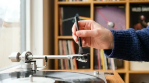 Gros plan sur une main utilisant une brosse en fibre de carbone pour nettoyer la pointe d'une platine vinyle.